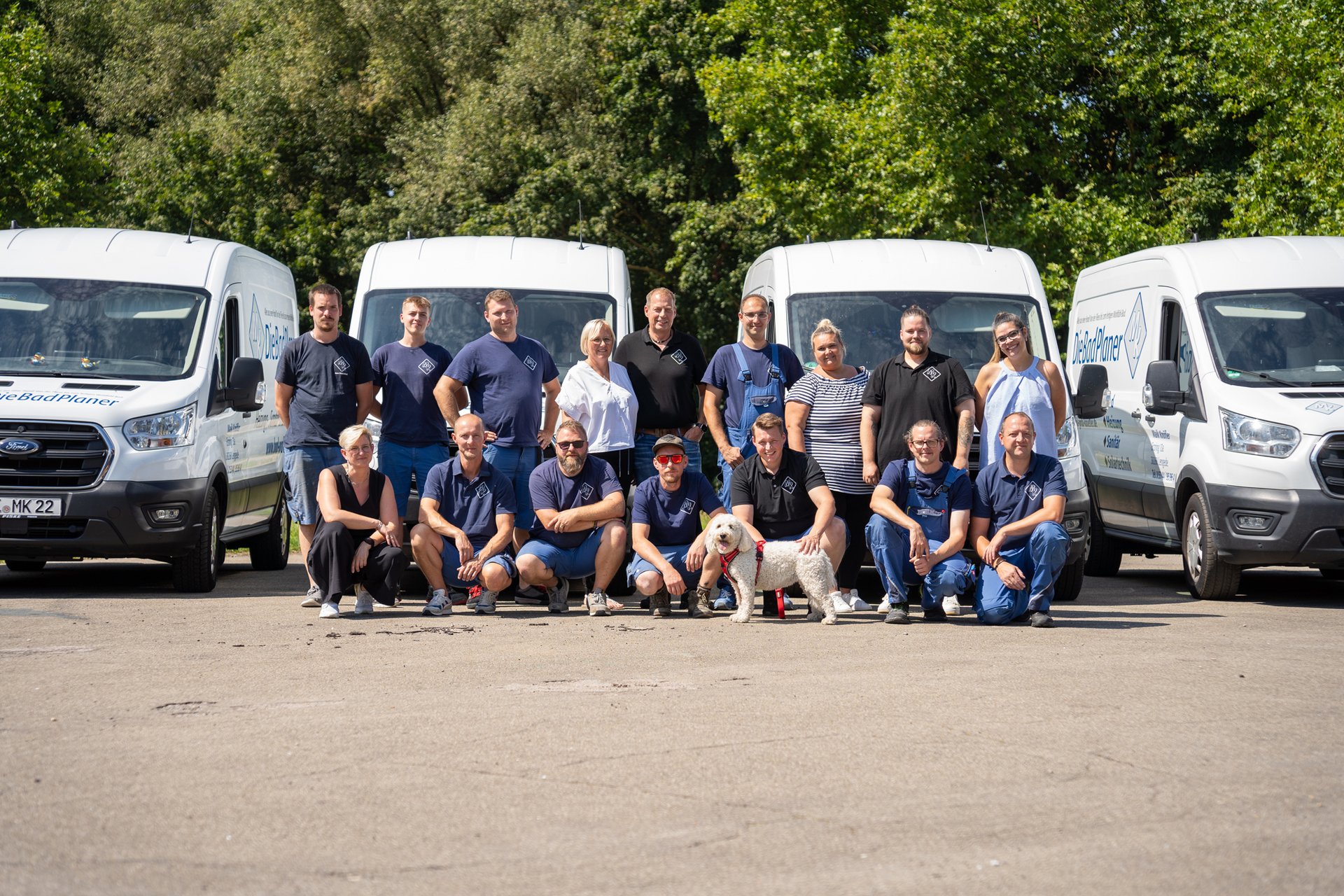 Das Team von „DieBadPlaner“ posiert vor vier weißen Lieferwagen an einem sonnigen Tag.